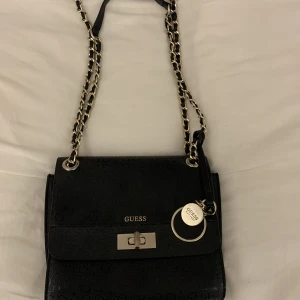 Guess väska  - Säljer min Guess väska som jag köpte i Italien. Den har rostat något på spännet (kan ses på bilden) så därav det låga priset. Går att töja ut så man får plats med relativt mycket och har bra med innerfack.   Kan användas som shoulder jag & crossbody bag. 
