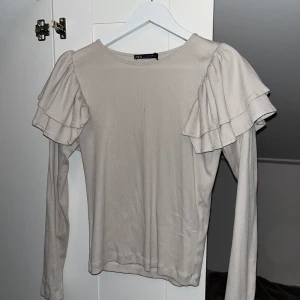 Beige Zara Tröja - En beige lite mer festlig långärmad tröja från Zara. Med volanger på axlarna. I strl L men skulle säga att den passar M och S också 