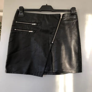 Minikjol i skinn - Minikjol i veganskt skinn strl s. Den stora dragkedjan är riktig och dom två små är för dekoration.