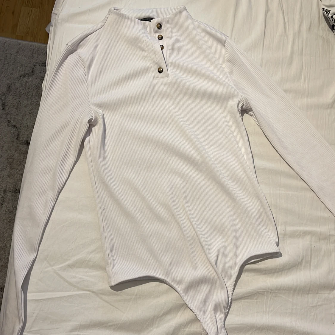 Vit långärmad body med knappar.