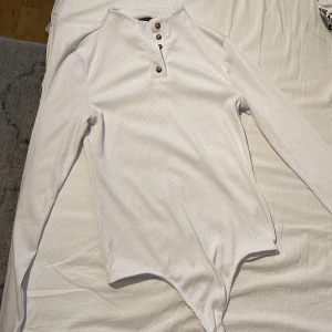 Vit långärmad body med knappar. - Vit långärmad body med knappar, storlek S, mjukt och strechigt material. Skön att ha på sig. 