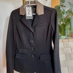 Tävlingskavaj Esperado - Helt oanvänd tävlingskavaj från Esperado, inköpt på SIHS, ny pris 149€. Svart kavaj i tåligt, lent och stretchigt material med en brunguldig krage. Prislapp och extraknapp sitter kvar. Storlek XS🫶🏼 skriv vid frågor eller för fler bilder