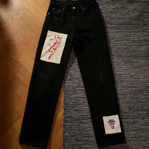 Svarta jeans med tryck  - Säljer dessa svarta jeans som är från chevy. Jag har målat båda figurerna som jag sedan sytt på jeansen. Storlek 36-38, så sitter lite baggy beroende på storlek. Hör av er vid frågor:) 