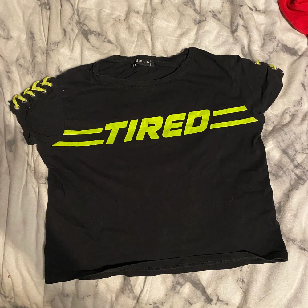 En svart t-shirt med grön text ”TIRED” och grön snörning på ärmarna. Stl M men skulle säga att de passar S bättre. T-shirts.