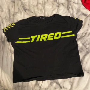 ”Tired” t-shirt - En svart t-shirt med grön text ”TIRED” och grön snörning på ärmarna. Stl M men skulle säga att de passar S bättre