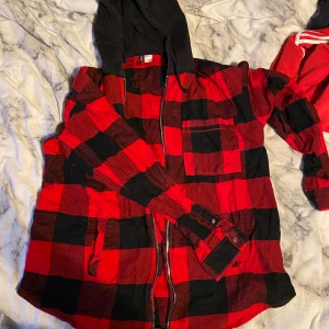 Flanell jacka/sip-hoodie - En flanell jacka/sip-hoodie från HM- divided med svart ”hoodie-luva”. En ficka på varje sida och en på vänstra bröstet