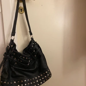 Svart axelväska!! - Så snygg axelväska med snygga spännen och nitar! Köpt seconhand och den är ganska använd men själv tycker jag det ser snyggare ut om det är använt än helt nytt i många fall! ❤️ stor och rymlig perfekt till skolan! Köparen står för frakt! Osäker på hur mycket frakten kostar dock!