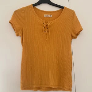 Gul Hollister t-shirt - Gul t-shirt från Hollister med knyte fram. Storlek M (passar nog S också) och i bra skick:)