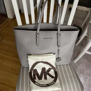 En grå Michael Kors Jet Set Leather Bag från 2019 i väldigt bra skick utöver handtagen som är lite smått slitna, utöver det är väskan i väldigt bra skick, detaljbilder finns. Förvaringspåse från MK ingår. 