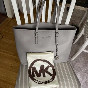 Michael Kors Jet Set Leather Bag Grå - En grå Michael Kors Jet Set Leather Bag från 2019 i väldigt bra skick utöver handtagen som är lite smått slitna, utöver det är väskan i väldigt bra skick, detaljbilder finns. Förvaringspåse från MK ingår. 