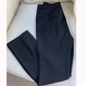 Svarta kostymbyxor med slits - Svarta kostymbyxor med liten slits på ”innersidan” av byxorna. Dem är köpta från Nelly, tyvärr för små för mig därav säljer dem. Superfint skick dem är knappt använda. Slutsålda på deras hemsida i denna storlek.