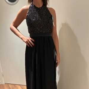 Festklänning till nyår - Långklänning med svarta paljetter och öppen rygg. Passar superbra till jul, nyår och bal!! Aldrig använd, helt ny från Nelly med lappen kvar✨skriv för fler bilder😚
