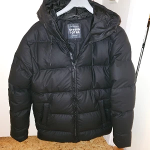 Dunjacka  - Dunjacka Waterproof Puffer Jacket från Studio Total Active. Varmt fodrad puffer med dunfyllning som är gjord i ett vattentätt yttertyg av PU-material vilket passar perfekt vid blötsnö. Passformen är regular. Testad inomhus,  strl S men passar M.