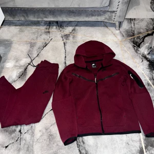 Nike tech vinröd - Säljer en jätte fin nike tech i färgen vinröd tyvärr är de en fläck på byxorna men det syns inte alls osedan är den lite fadead, detta är då inget märkvärdigt byxor S och kofta XS, den är använd sparsamt och köptes cirka 2,5 år sedan (äldre modellen)