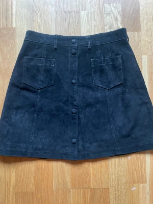 Mockakjol stl 36 - Använd en gång. Svart mocka. Knäppning hela vägen fram. A-linje formad. Storlek 36. 