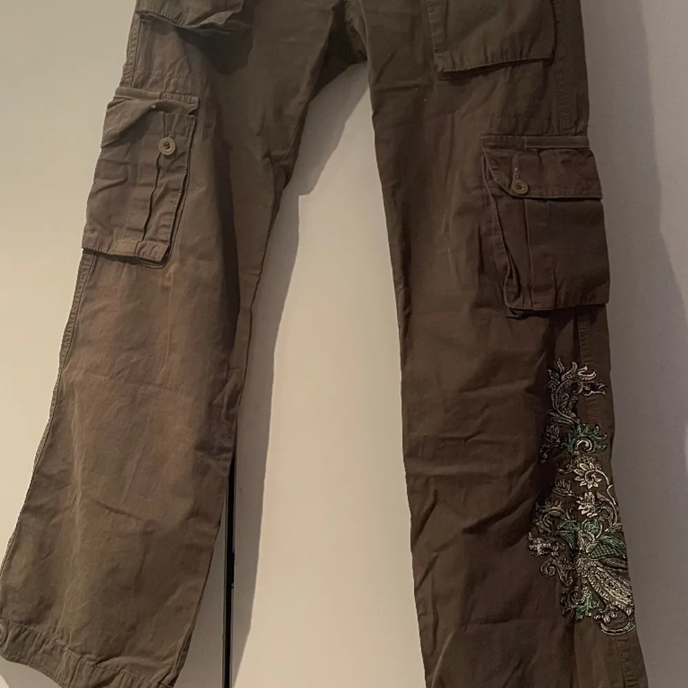 Lågmidjade cargopants stl 28 (midja). Färgen är brungrön. Broderi på höger ben. Jeans & Byxor.