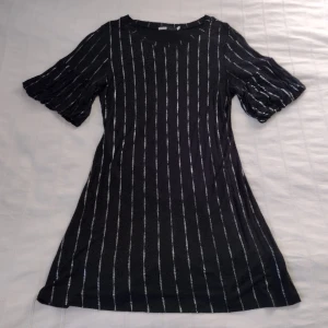 Svart klänning med silvrigt mönster och ballongärm  - Svart mjuk, stretchig och skön klänning med jättefint silvrigt mönster och fina vida kortare ärmar. Storlek L men passar fler storlekar, beroende på hur man vill att den ska sitta.