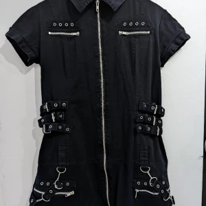 Kort klänning från Mercy L - En kort klänning ifrån märket Mercy, Väldigt bra skick, men har hängt oanvänd i en garderob i ett par år så kan behöva tvättas 😅  Har 4 äkta fickor framtill, kedjorna går att ta av,  och midjestrapsen går att justera. Rätt stretchigt tyg ✨