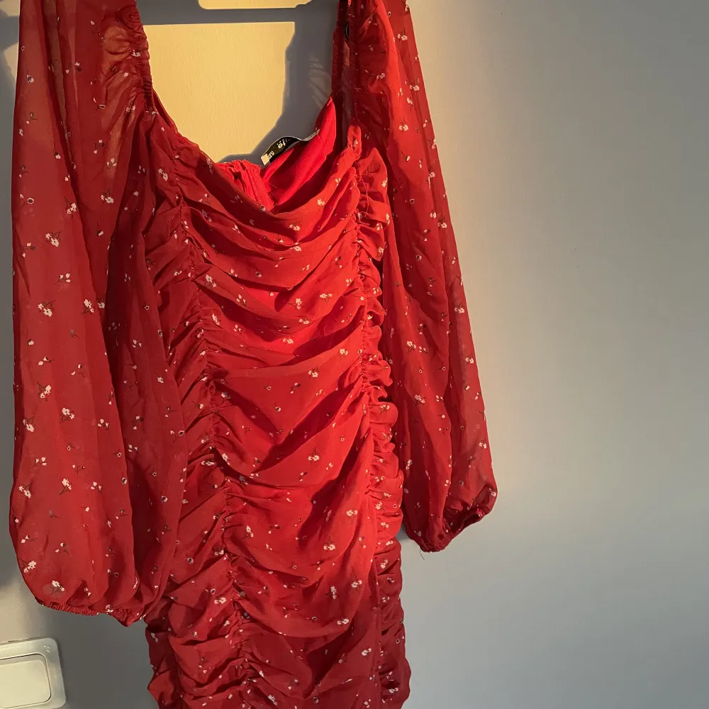 Röd klänning med blommönster. Dragkedja på ryggen. Tight och lagom kort med mesh material. . Mekot.