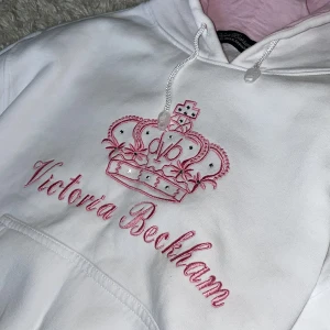 Vit & rosa Victoria Beckham hoodie - Säljer min vita Victoria Beckham hoodie med rosa detaljer. ❤️ Har snygga rhinestones på kronan och rosa luva. Storlek S. Köpare står för frakt! 💞