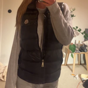 Monclerväst - Säljer min skitnsygga moncler väst då det inte riktigt är min stil längre. Den är ganska använd och har lite slitningar på ryggen men annars i väldigt fint skick, därutav det billiga priset. Jag har dock användt västen massor utan att tänka på slitagen!❤️