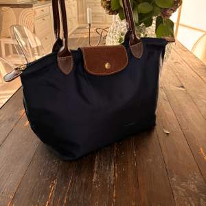 Longchamp väska i färgen marin blå, storlek medium. Väskan har några få defekter som syns på bild, (fram och baksida). Mått: 28 cm (L) x 26,5 cm (H) x 15,5 cm (W). Nypris 1350kr. Skriv för fler bilder vid intresse.🙏🏼