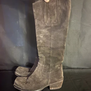 Damstövlar - Höga damstövlar i mocka, med en metalldetalj frampå. Klackens höjd: 5 cm.