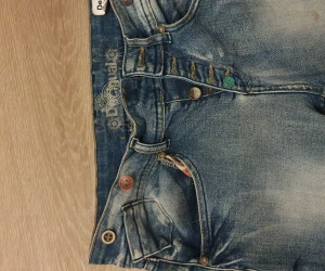 Desigual jeans. Nypris 1700. Säljes för 300. Översta knappen har lossnat. Och det finns en lite brun fläck.  - Desigual jeans. Strl 24, men stor i strl. Passar 26. Nypris 1700, säljes för 180 kr för översta knappen lossnat, går att bara sy på ny, och liten brun fläck.