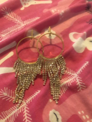 Guld glitter örhängen  - Ett par helt oanvända örhängen m glittrande stenar.  De är ca 4cm bereda & stenarna är va 4cm långa.  De är oanvända och har fått genomskinliga ploppar.  Kan betalas via Swish och skickas med vanlig post. 