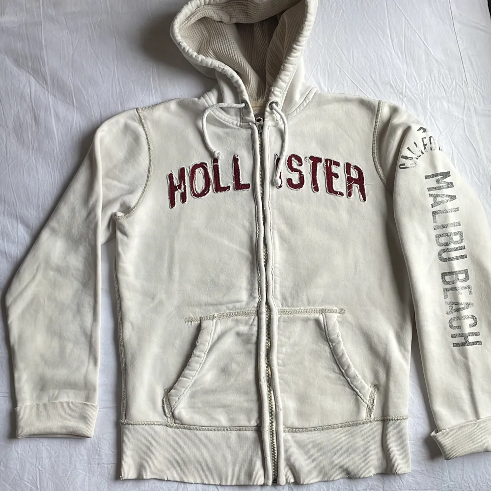 En vit Hollister zip-up tröja i utmärkt skick. Den är märkt som storlek S, men den kan bekvämt passa någon som normalt bär storlek M.. Hoodies.