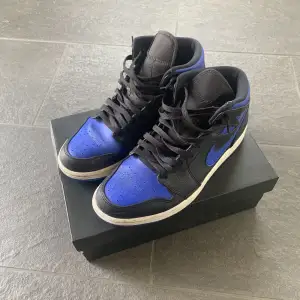 nike air jordan 1 mid i färgen black/hyper royal-white. använda under en sommar och sen dess aldrig använda. skorna är äkta och original box fås med såklart. cond 7/10 inga stora flaws, pris 400kr köparen står för frakt.