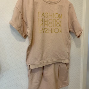 Det med sweatshirt och kjol från Pomp de Lux - Mysigt set med kortärmad sweatshirt och kjol från Pomp de Lux. Guldtryck på bröstet och invävda glittertrådar för mer lyster.  Kjolen är 33 cm lång mitt fram.  Stl 146/152. 