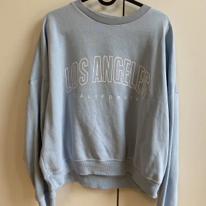 Ljusblå sweatshirt  - En ljusblå sweatshirt med tryck på framsidan. Använd ett fåtal gånger så den är som ny! Liten i storleken, brukar ha M/L i hoodien (gillar dom lite större) och denna är i XL. 