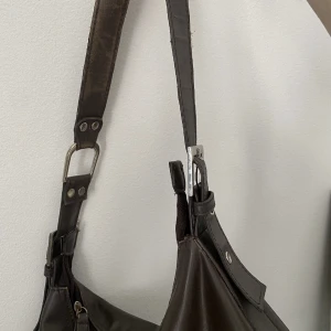 Mörkbrun väska - Superfin mörkbrun handväska i vintage/retro. Säljer då den inte kommer t användning. Skriv vid frågor eller om du vill ha fler bilder! Rymlig och perfekt storlek till vardags. Köp direkt: 500kr Mått: djup: 11 cm, höjd: 20 cm, bredd: 34cm