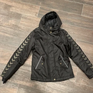 Hummel Vinterjacka - Hummel Vinterjacka i svart med guldtryck på ärmar. Jättefint skick