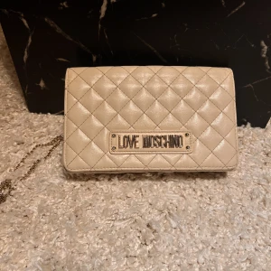 Krämvit moschino väska - Superfin väska från moschino, använt skick (visas på bild 2). Köpt för ca 1500kr mitt pris 450kr!