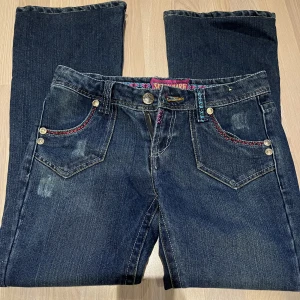 Lågmidjade utsvängda jeans med detalj - Säljer dessa lågmidjade jeans på grund av att jag köpte de av någon annan men de passade ej. De är utsvänga och har färgglada detaljer vid fickorna.  Midjemått - 40 cm  Innerbenslängden - 72 cm Jag är runt 160 och de passade på längden. 