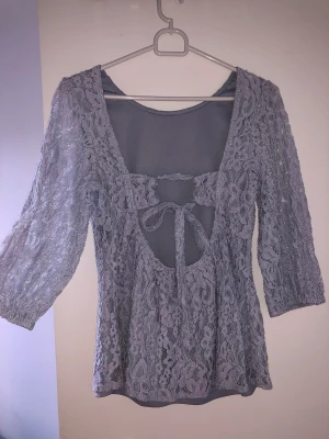 Ljusblå spetstopp - Ljusblå (EJ GRÅ) topp med spets och trekvartsärm. Låg rygg med detalj, går att knyta som man vill. NA-KD strl 36