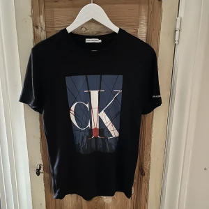 Calvin Klein T-shirt  - Jättefin svart Calvin Klein T-shirt med tryck på magen. Tröjan har används en del men den är väl omhändertagen så den har inga defekter. Skriv ifall ni har funderingar eller frågor.  Storlek EUR 170 men passar även S. Köparen står för frakten:)