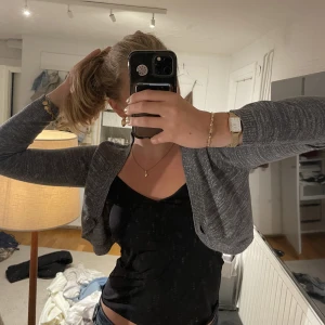 Stickad kofta med glitter - Snygg bolero/kort kofta med lite glitter i materialet. Färgen är typ en blandning av grå/grön/blå