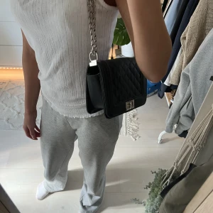 Svart handväska - Snygg svart handväska som har defekter under kedjan på båda sidorna (se bild) och vid spännet. Märks ej vid användning! Säljs då den ej kommer till användning.