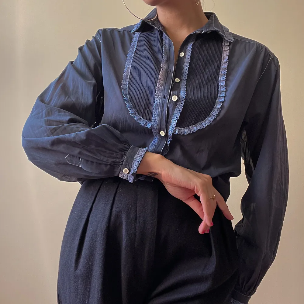 beautiful vintage women’s tuxedo shirt, hand dyed vintage in navy blue color  lace trims and pleated front details  puffy, cuffed sleeves for feminine effect with white button closure  unique piece, some natural dye discoloration & a tiny pinhole in left . Blusar.