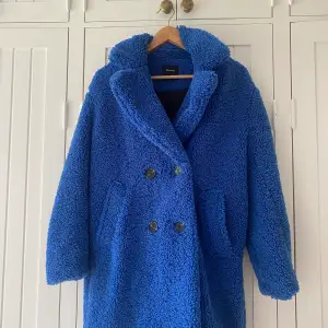 Bershka blå kappa i bra kvalite. Varm jacka, fluffig, går att knäppa på olika sätt