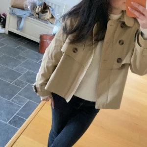 Skit snygg kort trenchcoat  - Jättefin trenchcoat från hm i storlek 34. Liten i storlek jag är storlek 32 för referens. Passar även 34 men blir en tightare modell då. Jättefin och sparsamt använd. Den är randig inuti men inget som syns när man har på sig den. Finns inte att köpa längr