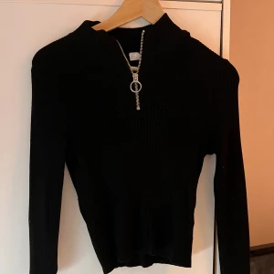 Svart tröja med dragkedja  - Svart ribbad långärmad tröja med dragkedja. Använts många gånger men fortfarande bra skick och inga skavanker