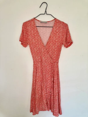 Midsommar klänning  - Super söt klänning i XS från pull&bear, röd med vita blommor. Material i bomull. Modell som omlottklänning. Längd mini Skicket är perfekt 