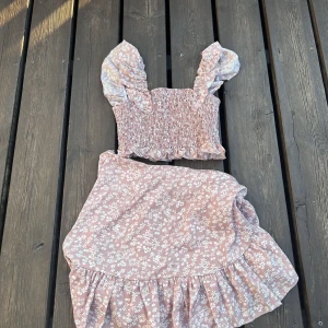 Blommigt set  - Ett mycket fint oanvändt set!  Kjolen är justerbar, något kortare än vanliga kjolar.  