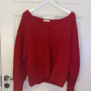 Stickad tröja - En röd stickad tröja med v ringad hals och långa armar. Armarna är tightare längre ner än vad de är uppe på armen.