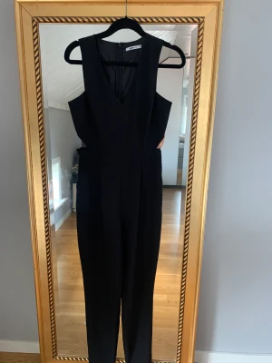 Byxdress cutout  - Svart byxdress med cutouts från Gina. Byxorna är mer åt kostymhållet. Avsmalnande nertill. 