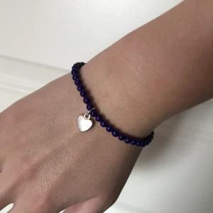 Vackert pärlarmband  - Vackert pärlarmband av fossil sten, polerade och behandlade med hög glans. Har ett silverhjärta hängande på sidan av armbandet. Nytt oanvänt och handgjort. Kontakta gärna vid frågor. Har också fler smycken på min profil. Marinblå- lila.